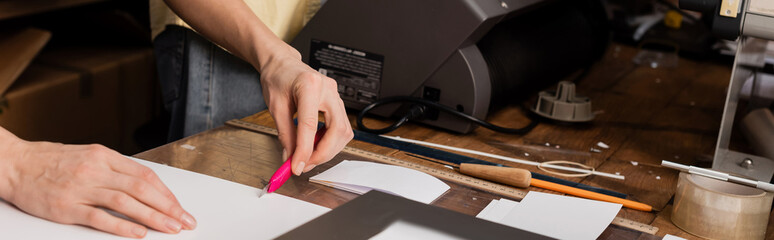 cropped view of typographer cutting paper with knife in print center, banner.