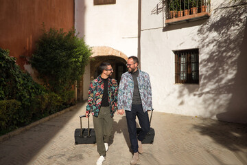 Real marriage of gay couple, holding hands, walking around the city with a travel suitcase in the...
