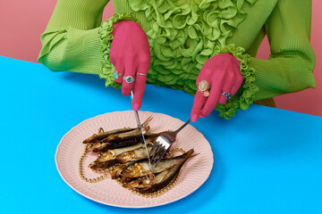 Portrait of stylish woman wearing gold rings holding food utensils eating fish at the blue table. Trash pop art, bright colors