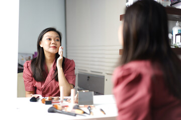 Beautiful Asian woman doing makeup in front of a dressing table mirror