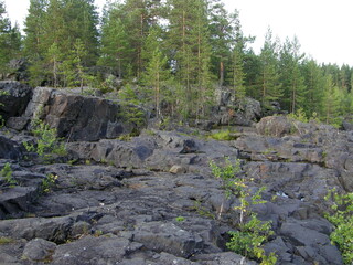 A rocky landscape with trees and rocks in the foreground. Waterfall Poor Porog, Girvas, Republic of Karelia, Russia.