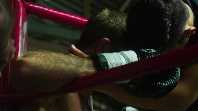 4K Cinematic slow motion footage of a Muay Thai coach pouring water on his fighter and massaging his body on a boxing ring during a Muay Thai boxing fight in a stadium