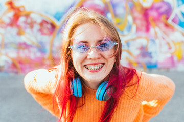 Portrait of a young laughing girl with braces listening to music in headphones in the summer on the...