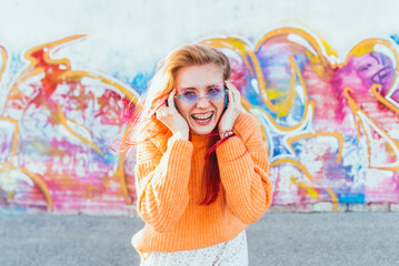 Portrait of a young laughing girl with braces listening to music in headphones in the summer on the street