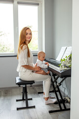 Mother and baby daughter playing piano. Baby development. Sensory experience. Early years.