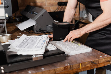 partial view of man in apron checking quality of newspaper through magnifying glass in print center.