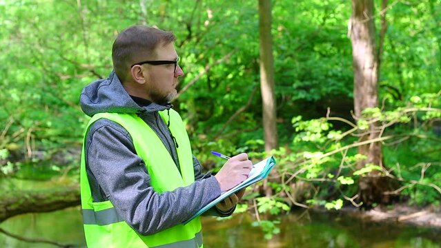 Male ecologist makes records of the state of the environment forest river. Environmental control.