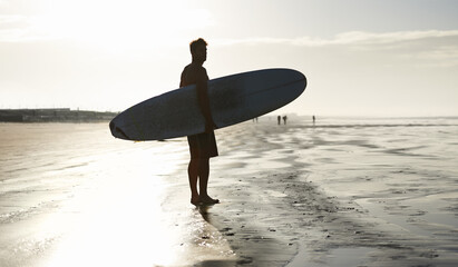 Fototapeta na wymiar Waiting for the tide to come in. A handsome young surfer at the beach craving a good wave.