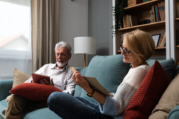 Simple living. Happy middle-aged senior couple 70s husband and wife sit relax on couch in living...