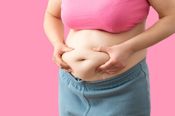 Close up of a obese young woman checking her fats against a pink background