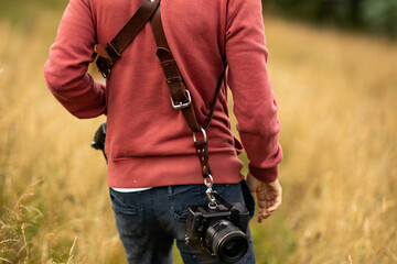 photographer sits with his back to the camera, clad in a leather camera harness and surrounded by...