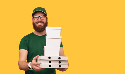 Studio shot with copy space of a delivery man holding some lunch boxes over yellow background.