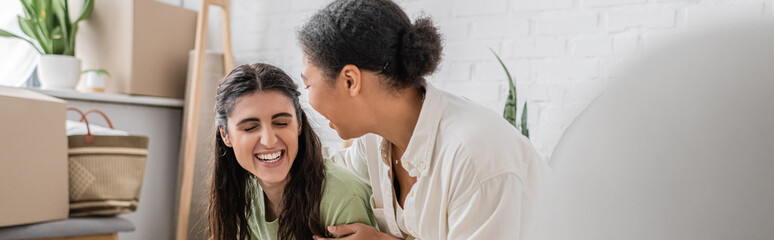 happy interracial lgbt couple laughing in new house, banner.