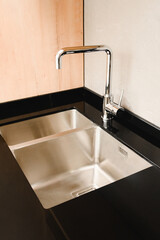 Metallic sink without dishes. Clean sink in the kitchen. House cleaning. Kitchen after renovation. Faucet and sink in the kitchen after installing an unknown label