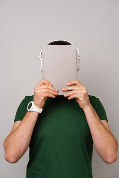 Vertical shot of a man covering his face with a journal or book cover while wearing headphones.