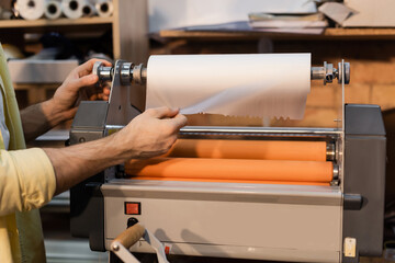 cropped view of worker pulling paper while working with print plotter.