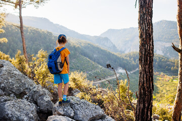Naklejka premium Traveling child. a tourist with a backpack stands on a mountain path looks at the mountains. hiking and active healthy lifestyle.