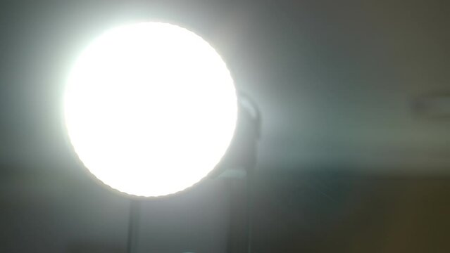 Close-up panning shot of professional aputure videographer lamp in darkness indoors. Bright light shining in equipment
