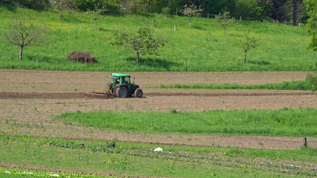 Green tractor ploughing agriculture field on a sunny spring day at City of Zürich district Schwamendingen. Movie shot May 4th, 2023, Zurich, Switzerland.