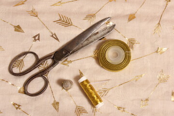 Spool of Gold Thread and Scissors With Thimble on Metallic Fabric