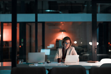 Putting her career first. a businesswoman using a laptop at her desk during a late night at work. - obrazy, fototapety, plakaty
