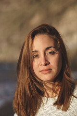 Caucasian woman with brown hair and white shirt on the beach at sunset.
