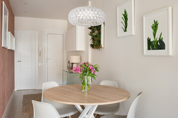 Entrance hall dining room with a round wooden table, white chairs and paintings in the interior of...