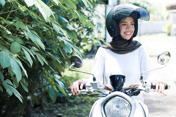Young Asian muslim woman riding motorcycle wearing helmet
