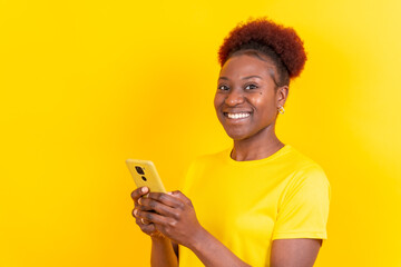 Young african american woman isolated on a yellow background smiling with the mobile phone, study session