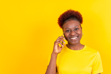 Young african american woman isolated on a yellow background smiling with the mobile phone, study session