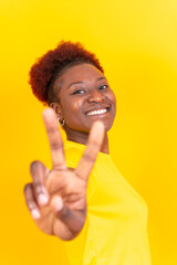 Young african american woman isolated on a yellow background smiling with the victory gesture, studio shoot