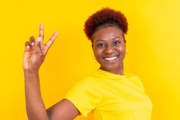 Young african american woman isolated on a yellow background smiling with the victory gesture, studio shoot