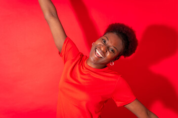 Fototapeta na wymiar Young african american woman isolated on a red background smiling and dancing, studio shoot