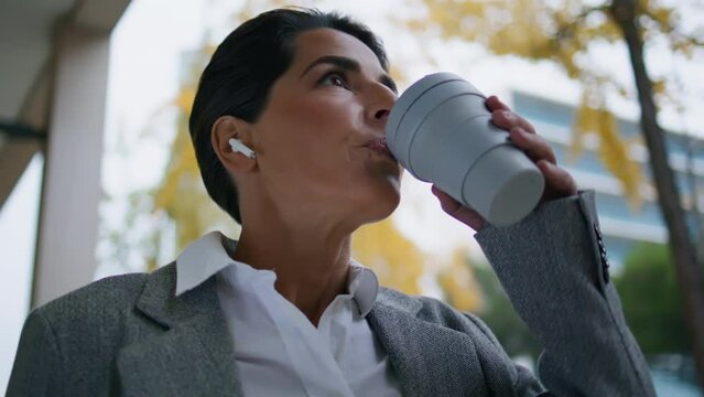 Walking businesswoman listening music in earpods closeup. Relaxed manager drink
