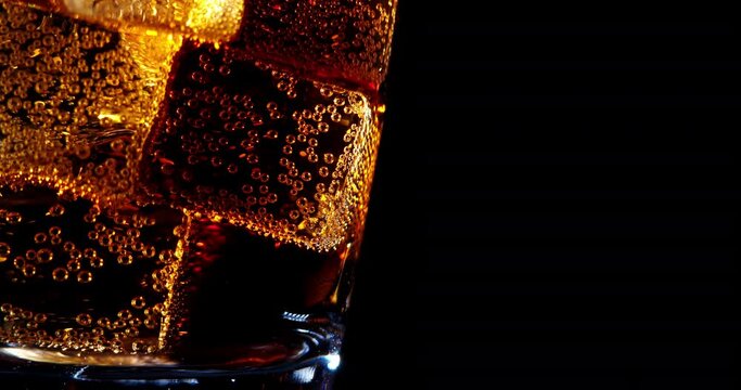 Pouring Cola with ice cubes close-up. Cola with Ice and bubbles in glass. Coke Soda closeup. Food background. Rotate glass of Cola fizzy drink over brown background. Slow motion 4K UHD video footage