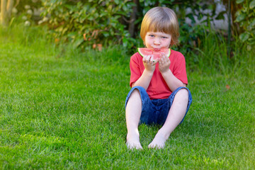 little boy eats watermelon sitting on grass in the park