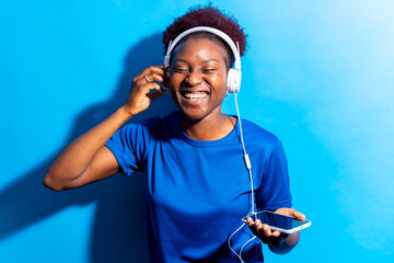 Young african american woman isolated on a blue background with headphones dancing, studio shoot