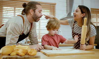 Father and mother teaching baby son kneading dough on kitchen counter at home. Parents and boy kid enjoy and fun indoors activity cooking together.