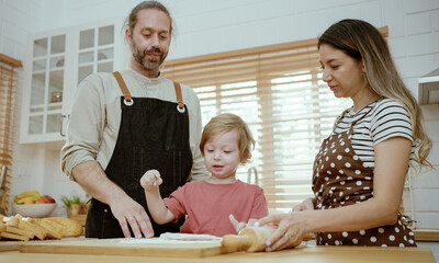 Father and mother teaching baby son kneading dough on kitchen counter at home. Parents and boy kid enjoy and fun indoors activity cooking together.