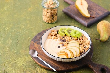 Breakfast, granola with yogurt, pear, kiwi and raspberries in a flat white plate on a green concrete background. Healthy quick breakfasts.