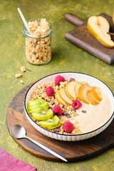 Breakfast, granola with yogurt, pear, kiwi and raspberries in a flat white plate on a green concrete background. Healthy quick breakfasts.