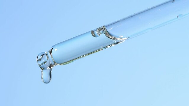 Glass dropper with dripping essential oil on a blue background, macro. Beauty background with a means for massage.