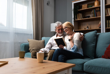 Two elderly people senior couple man and woman looking at a family photo smile and hug while...