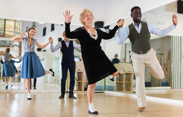 Man and elderly woman performing jazz dance in dancing room