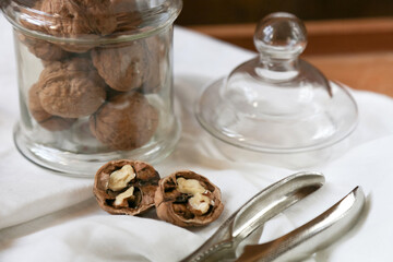 Two walnut halves and a glass can of nuts in blurry focus are on the table surface next to the...