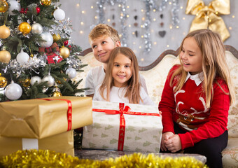 Fototapeta na wymiar Two girls and boy holding gift in Christmas interior