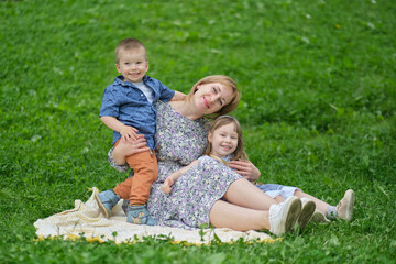 Cherished memories: A woman in her middle years lovingly holds her children close as they sit on a blanket in the park, creating lasting memories together.