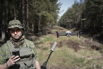 Fototapeta premium A military scout with a rifle with a silencer controls a drone in the forest.