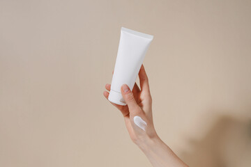 Female hand with smear holding blank mockup tube of cream on beige isolated background. Daily...