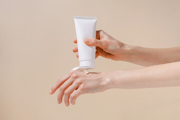 Female hands squeeze moisturizing cream from a white blank tube. Concept of cosmetology and natural skin care products. Mockup for your design.